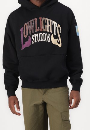 Schwarzer Kapuzenpullover mit mehrfarbig besticktem Text "LOWLIGHTS STUDIOS" in verschiedenen Schriftarten und einem kleinen blauen Etikett am Ärmel.