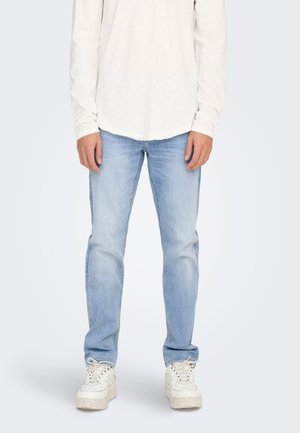 Jeans de mezclilla azul claro con corte recto, combinados con una camiseta de manga larga color crema y zapatillas blancas. Textura suave, diseño casual.