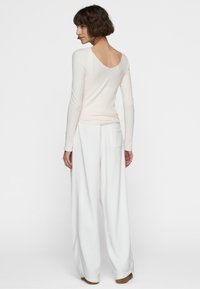 Top a maniche lunghe a costine in beige chiaro con scollo rotondo, abbinato a pantaloni bianchi a gamba larga con tasca posteriore.