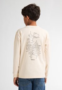 Beige Langarmhemd mit einem schwarzen Grafikdesign von Bäumen und Text auf der Rückseite. Aus Baumwolle mit Rundhalsausschnitt gefertigt.