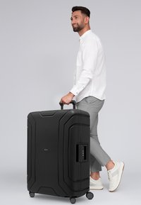 Schwarzer Hartschalenkoffer mit strukturierter Oberfläche, ausgestattet mit einem Zahlenschloss, einem ausziehbaren Griff und vier drehbaren Rädern für Mobilität.