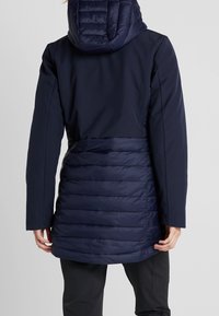 Marinblå tvåfärgad kappa med vadderad nederdel och slät övre tygdel. Har huva och långa ärmar med sidoseamsdetalj.