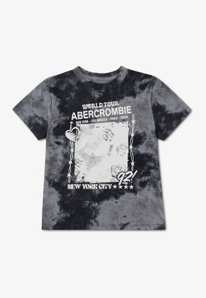 T-shirt tie-dye noir et gris avec le texte "Abercrombie World Tour" et un visuel représentant une guitare, des roses et des villes comme New York et Tokyo.
