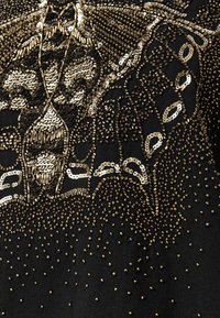 Tela negra con intrincados bordados de lentejuelas y cuentas doradas. Presenta patrones florales y geométricos, creando un diseño texturizado y detallado.