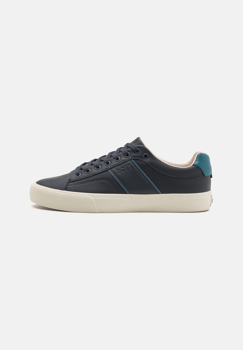 Donker marineblauwe leren sneaker met een lichtgrijze zool, voorzien van teal-stripes en vijf gaatjes voor veters. Minimalistisch ontwerp met een gevoerde kraag.
