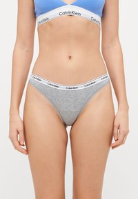 Grå bomullstanga med hvit elastisk midjebånd som har "Calvin Klein"-logo. En enkel design, glatt tekstur og tettsittende form.