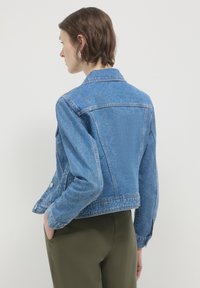 Giacca di jeans azzurra, con maniche lunghe, colletto e chiusura con bottoni. Il retro presenta un taglio sagomato e dettagli di cucitura sottili.