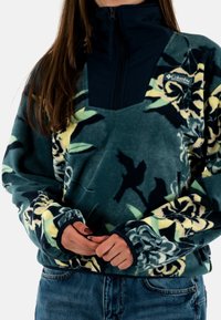 Sudadera de forro polar en verde con patrones florales en amarillo y negro. Cuenta con un cuello alto y cierre de cremallera, mangas y bolsillo en un azul marino contrastante.