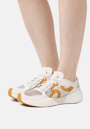 Hvide og orange atletiksneakers med mesh- og gittermønstre, båret på bare fødder, vist fra siden og let ovenfra på en hvid baggrund.