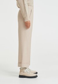 Kahvin väriset muotiluodut housut, joissa on suora leikkaus ja taitettu helma, yhdistettynä vaalean kahvin värisiin vaelluskengiin, joissa on hopeiset yksityiskohdat ja mustat pohjat.