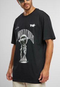 T-shirt en coton noir avec impression graphique d'un globe en argent et des figures. Col rond, manches courtes, avec un logo blanc sur la poitrine.