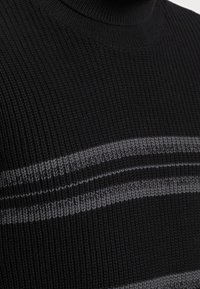 Maglione nero a coste con collo alto, caratterizzato da strisce orizzontali grigie sulle spalle, realizzato in materiale di maglia testurizzata.