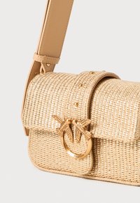 Woven straw bag in beige with a curved flap, decorative bird-shaped clasp, and a leather strap. Textured surface with gold accents.