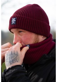 Bordeauxfarbene gestrickte Mütze mit Ripptextur und passendem Halswärmer. Beide Artikel sind mit einem kleinen Logopatch versehen. Weiches, gemütliches Material.