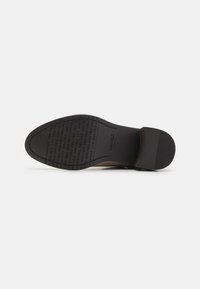 Black rubber sole with textured grip, featuring branded lettering. The heel is slightly raised, providing a structured, defined shape.