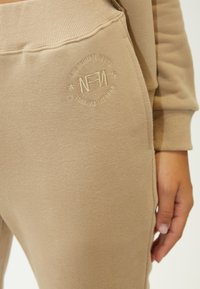 Beige Jogginghose aus weichem Stoff, mit strukturiertem Finish und gesticktem Logo an der Seite. Elastischer Bund für Komfort.