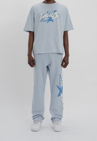 Camiseta de algodón oversize color azul claro con estampado gráfico y pantalones de chándal a juego en azul claro. Zapatillas blancas completan el conjunto.