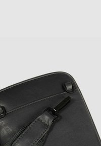 Schwarze Ledertasche mit glatter Textur, abgerundeter Form, sichtbaren Nähten und einem eleganten Metallbeschlag.