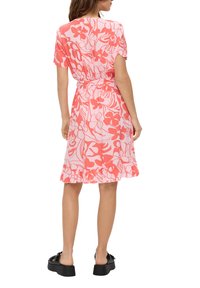 Kleid mit Blumenmuster in Pink und Koralle, aus leichtem Stoff, kurze Ärmel, Taillengurt, geraffter Saum, getragen mit schwarzen Plateau-Sandalen.