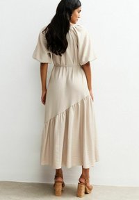 Beige maxi-jurk met korte poffmouwen, gestructureerde stof en tiered ruches aan de onderkant. Gepaard met chunky sandalen met kurk hakken.
