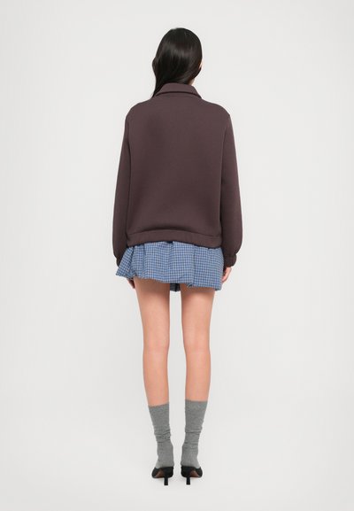 Καφέ φλις φούτερ με ψηλό γιακά, σε συνδυασμό με μπλε καρό μίνι φούστα και γκρι κάλτσες μέχρι το γόνατο, φορεμένο με μαύρες γόβες.