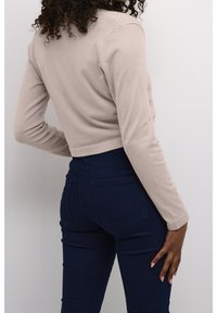 Beige verkürzter Pullover mit langen Ärmeln und geripptem Muster. Kombiniert mit dunkelblauen, eng anliegenden Jeans mit Gesäßtaschen.