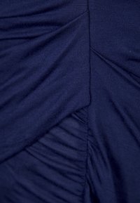 Námořnická modrá látka s nabranými sekcemi a svislým stehováním. Měkká textura s mírným leskem, vytvářející vrstvený vzhled.