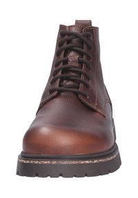 Bota de cuero marrón con un exterior texturizado, punta redondeada, parte delantera con cordones y suela de goma resistente. Presenta un tacón ligeramente elevado.