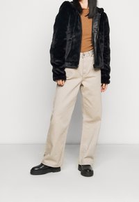 Black faux fur zip-up jacket with a hood, worn over a brown ribbed top and beige wide-leg pants. Black platform boots complete the outfit.