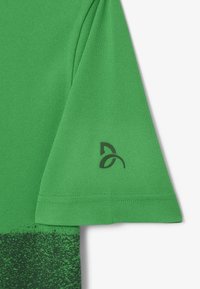 Grön polo t-shirt med texturerad tyg, korta ärmar och en svart logotyp på ärmen med ett gradientmönster vid nederkanten.