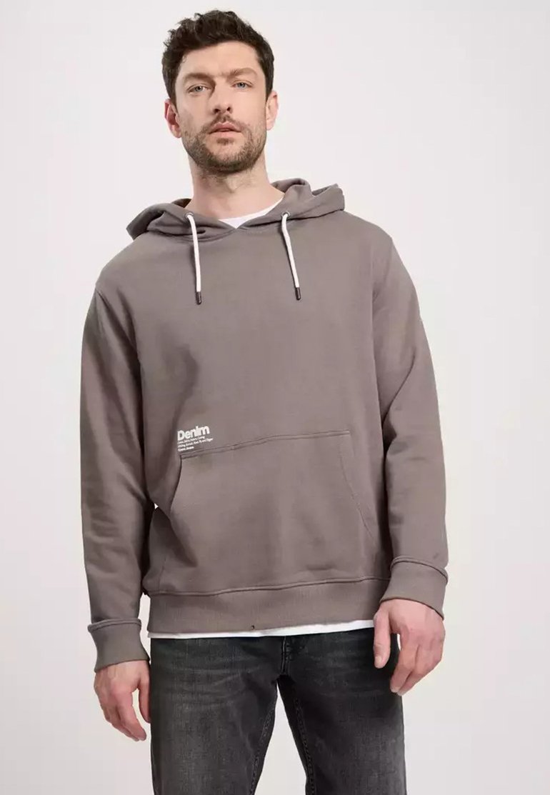 Szara bluza z kapturem z miękkiego materiału. Posiada przednią kieszeń, ściągacz przy kapturze oraz małe logo po lewej stronie. W połączeniu z ciemnymi dżinsami.