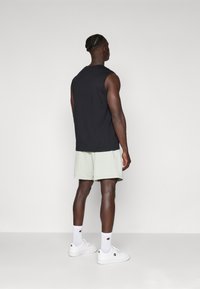Top negro sin mangas combinado con pantalones cortos verdes claros. Zapatillas blancas y calcetines hasta el tobillo. Textura suave, corte relajado y diseño minimalista.