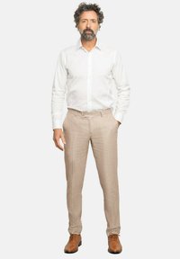 Camisa de vestir blanca de manga larga, pantalones de tejido beige, y zapatos de cuero marrón. Los pantalones tienen un corte entallado y un sutil patrón a cuadros.