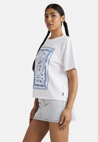 Witte katoenen t-shirt met een blauwe grafische print van botanische motieven. Boxy vorm met korte mouwen en een lichte verlenging van de zoom.