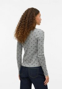 Grå långärmad tröja med ett subtilt hjärt-mönster i brunt. Har en figurnära design och mjuk textur. Kombinerad med mörka jeans.