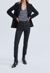 Black leather pants with detailed stitching, paired with a gray v-neck sweater and a structured black blazer, and shiny black ankle boots.