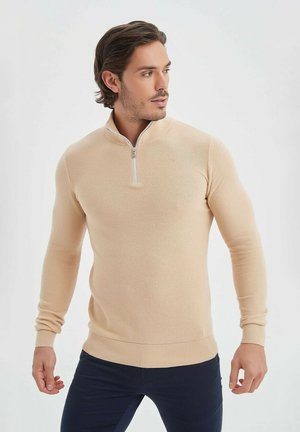 Pull beige à demi-zip avec un design en tricot texturé, manches longues, poignets et ourlet côtelés. Un accent en zip au col ajoute une touche de détail.