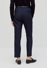 Marineblauwe op maat gemaakte broeken van gladde stof, met een slim fit, zijzakken en een zwarte riem. Platte voorkant zonder zichtbare patronen.