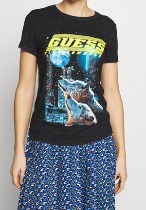Black cotton t-shirt featuring a graphic of wolves against a city skyline and moon, with "GUESS" in bright yellow text.