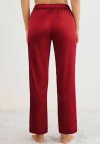 Bordeaux satijnen pyjamabroek met een elastische tailleband, rechte benen en opgerolde manchetten. Glad van textuur zonder aanvullende patronen.
