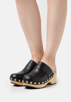 Zwarte leren klompen met een ronde neus, voorzien van gouden studs langs de houten zool en een verhoogd plateau, instapontwerp en gestructureerde bovenkant.