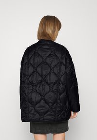 Black quilted jacket with a loose fit, featuring a textured pattern and a round neckline. Smooth fabric and dropped shoulders.