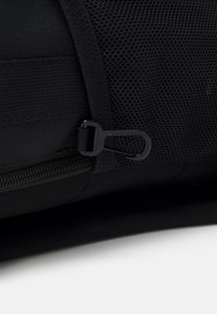 Svart tygväska med en strukturerad mesh-panel, en dragkedja med en elegant svart dragflik och förstärkta sömmar för hållbarhet.