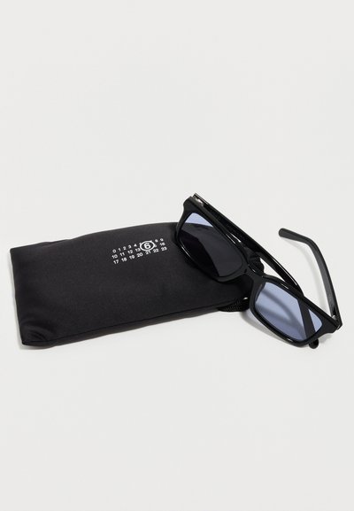 Black rectangular sunglasses resting on a black fabric pouch with white numeric logo on a white background.