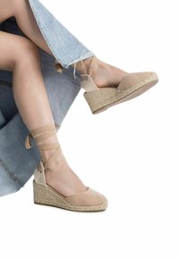 Wedges de esparto de ante beige con acentos trenzados, suela de yute y tiras de tobillo entrecruzadas. Los jeans presentan detalles de dobladillo deshilachado.