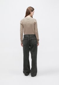 Bež majica z dolgimi rokavi, kombinirana z visokim pasom temno sivih širokih kavbojk z dvema zadnjima žepoma in gladko teksturo.