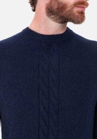 Pull en maille bleu marine avec un col rond et un motif torsadé vertical au centre. Texture douce et coupe ajustée.