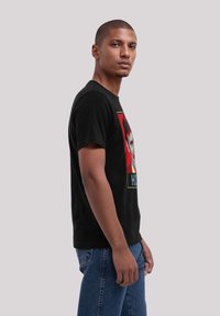 Black t-shirt featuring a colorful graphic print on the front. Short sleeves, standard crew neck, and relaxed fit. Blue jeans visible.