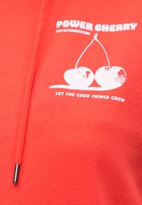 Κόκκινο φούτερ από μαλακό ύφασμα με γραφικό δύο κερασιών και κείμενο "POWER CHERRY 100% FRESHNESS" σε λευκό τύπωμα.