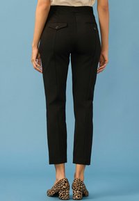 Schwarze, maßgeschneiderte Hose mit hoher Taille, zwei Gesäßtaschen mit Knöpfen und schmaler Passform, kombiniert mit Schuhen mit Leopardenmuster.